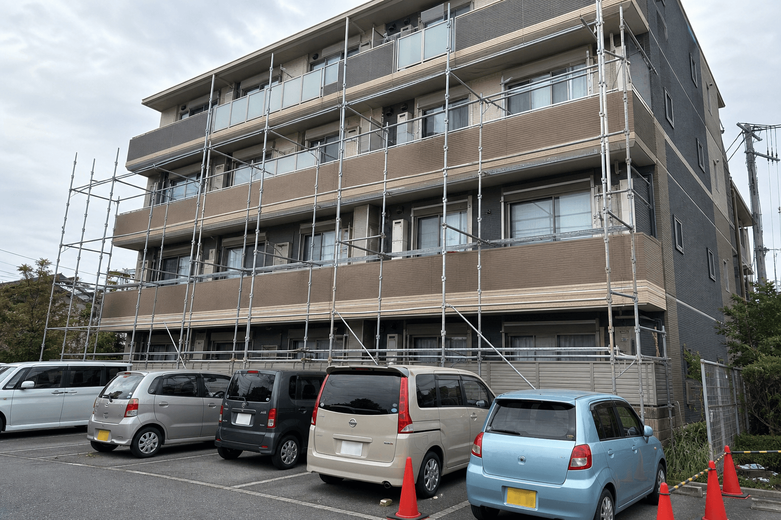 足場組立中の建物直下に複数の車両が駐車している架空の現場例